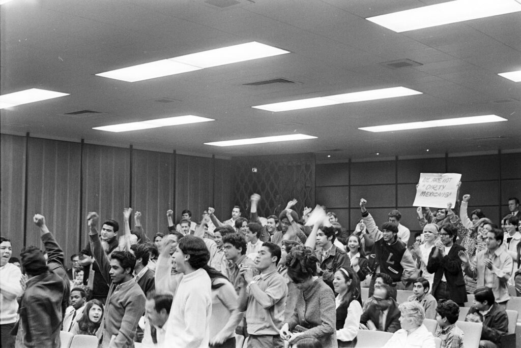 Black and white photo of students raising their fists during an LAUSD Board of Education Meeting in 1969.