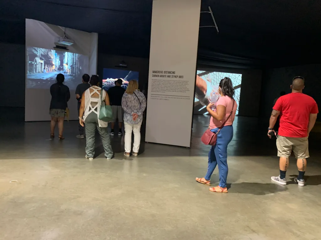 Photograph of LA Art Show attendees viewing video installations in a dark gallery space.
