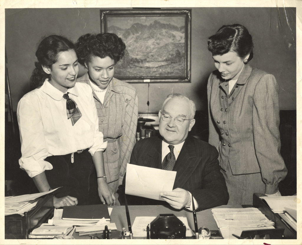 Black and white photo of LA Mayor Fletcher Bowron sitting at his desk with three members of the Panel of Americans in 1945.