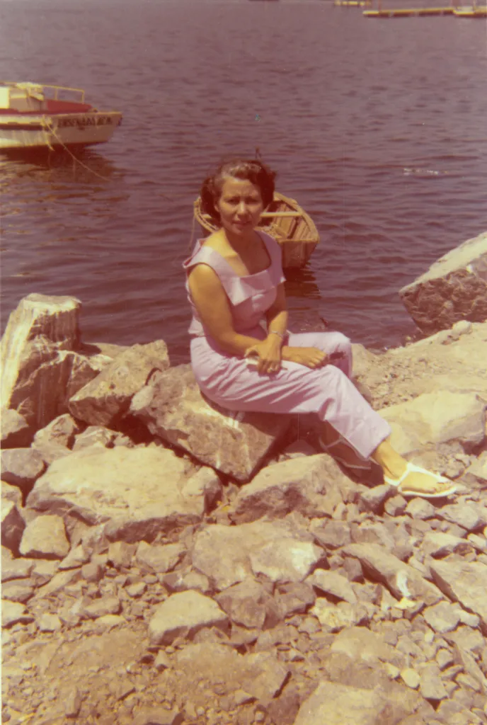 Colorful photograph of Josefa Serna sitting on rocks beside the water in Ensenada, Baja California, Mexico, in 1957.