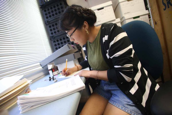 Photo of Lupe Sanchez sitting at a desk and working with documents from the Moctesuma Esparza Collection.