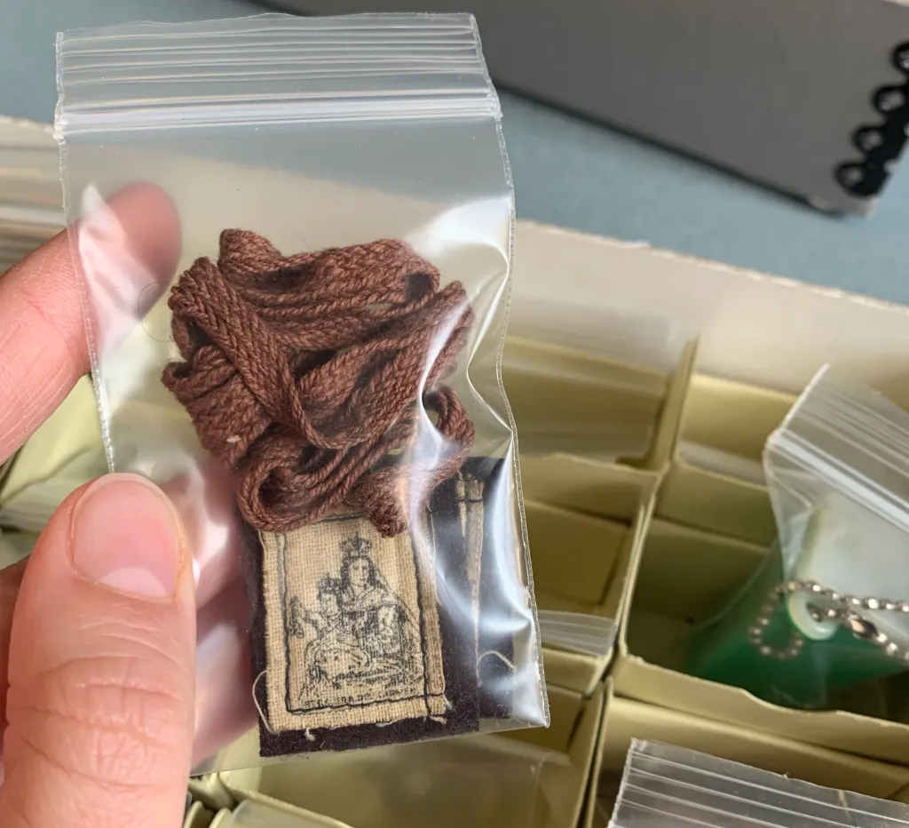Color photograph of a brown religious scapular inside a clear plastic bag held by a person's hand.