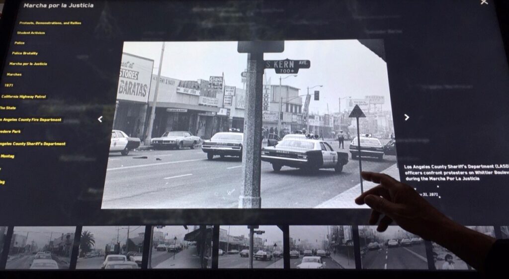 Photo of a digital archive showing a black and white photo of police cars during the Marcha Por La Justicia.